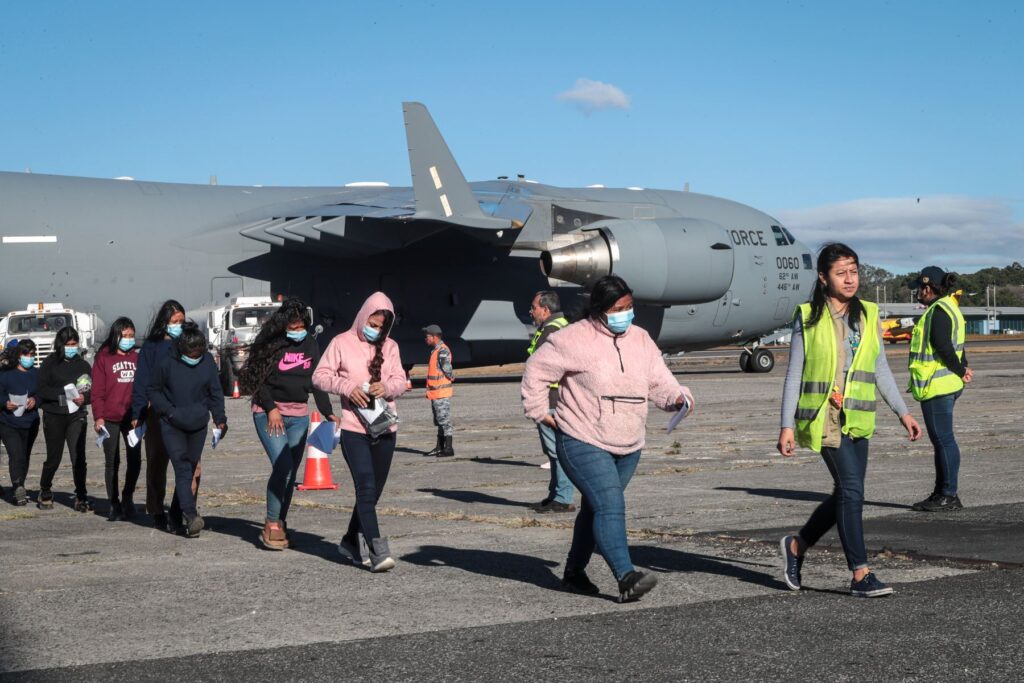 Personas caminando junto a un avión militar gris.