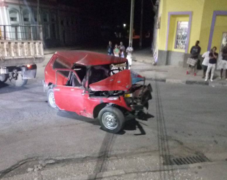 Accidente coche rojo con camión por la noche.