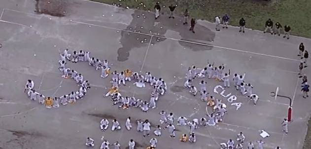 Personas forman las palabras SOS Cuba en el suelo.