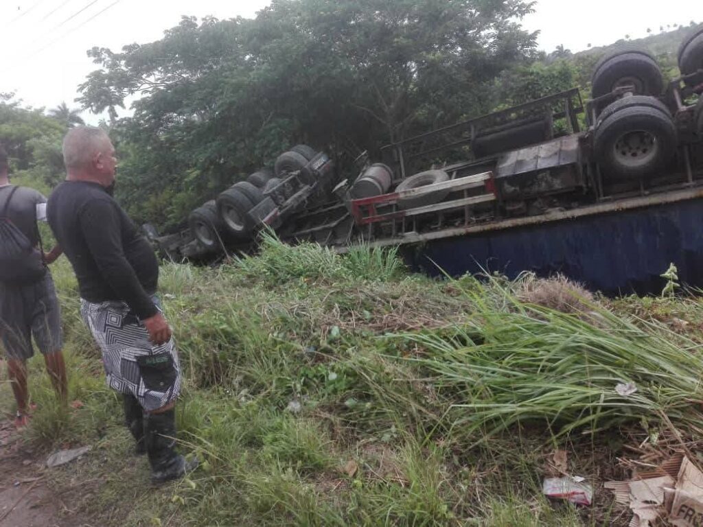 Camión volcado en la carretera, personas observando.