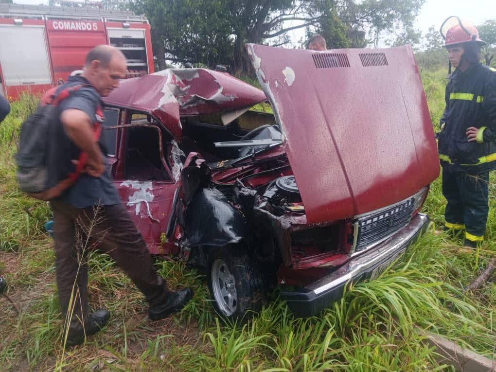 Bomberos inspeccionan coche accidentado rojo en la carretera.