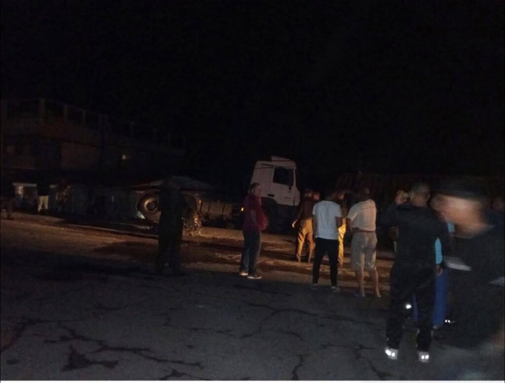 Accidente nocturno con camión volcado y personas alrededor.