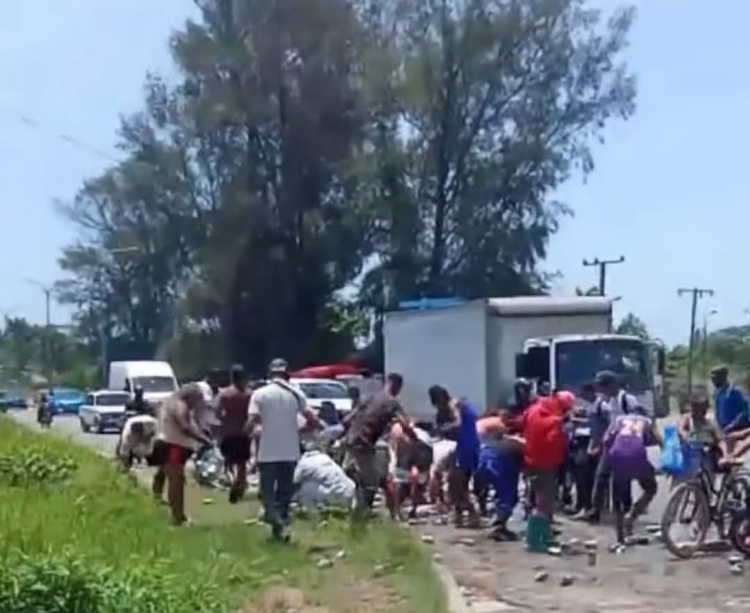 Personas recogiendo objetos de un camión volcado