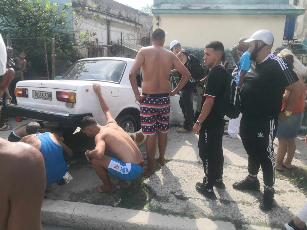 Grupo de personas arreglando un coche blanco en la calle.