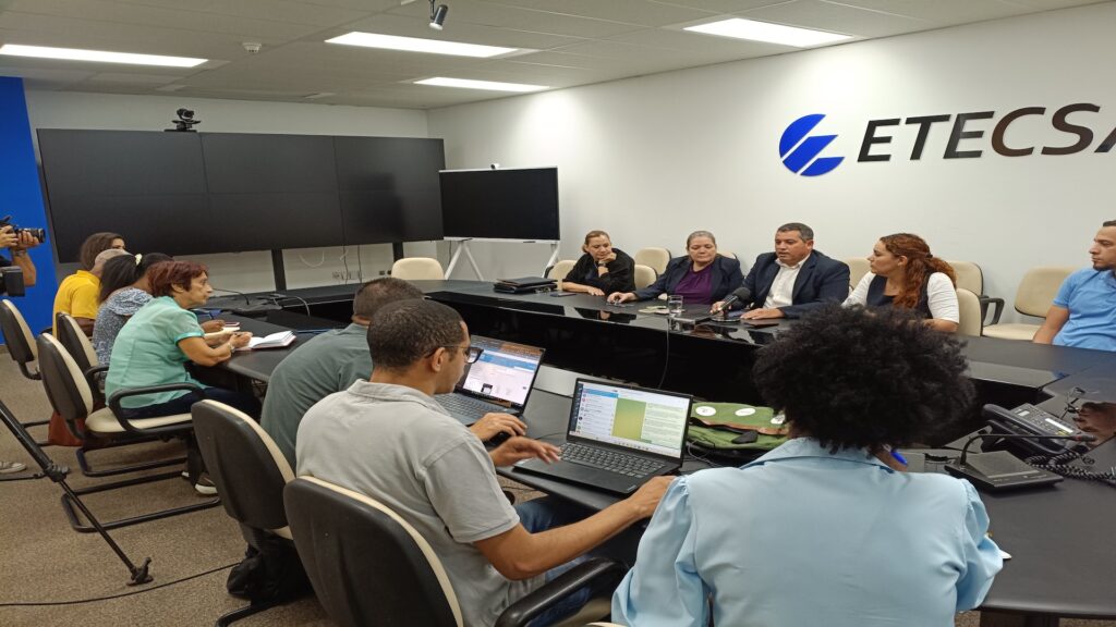 Personas en reunión de oficina con laptops y pantallas.