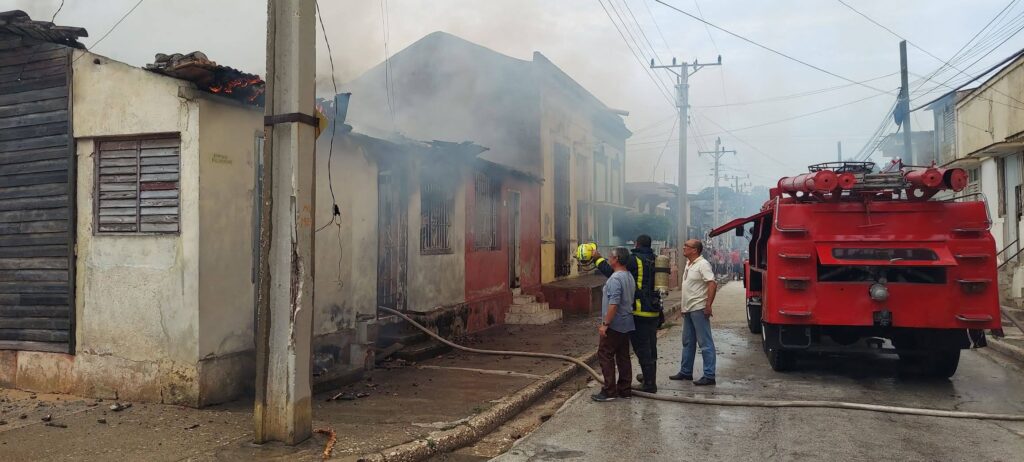 Incendio en casa, bomberos trabajando, camión rojo cerca.