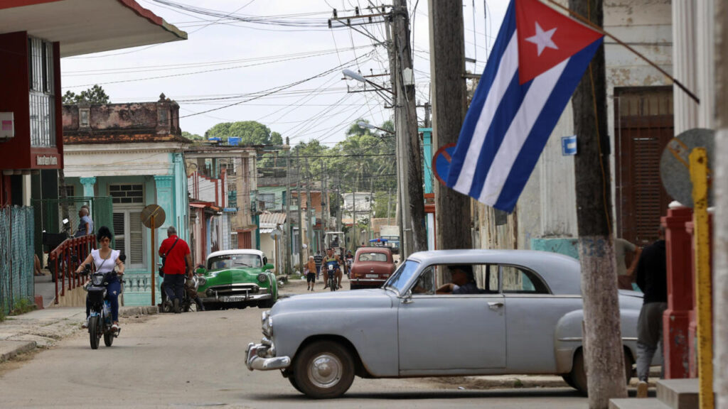 Calle cubana con coches clásicos y bandera.