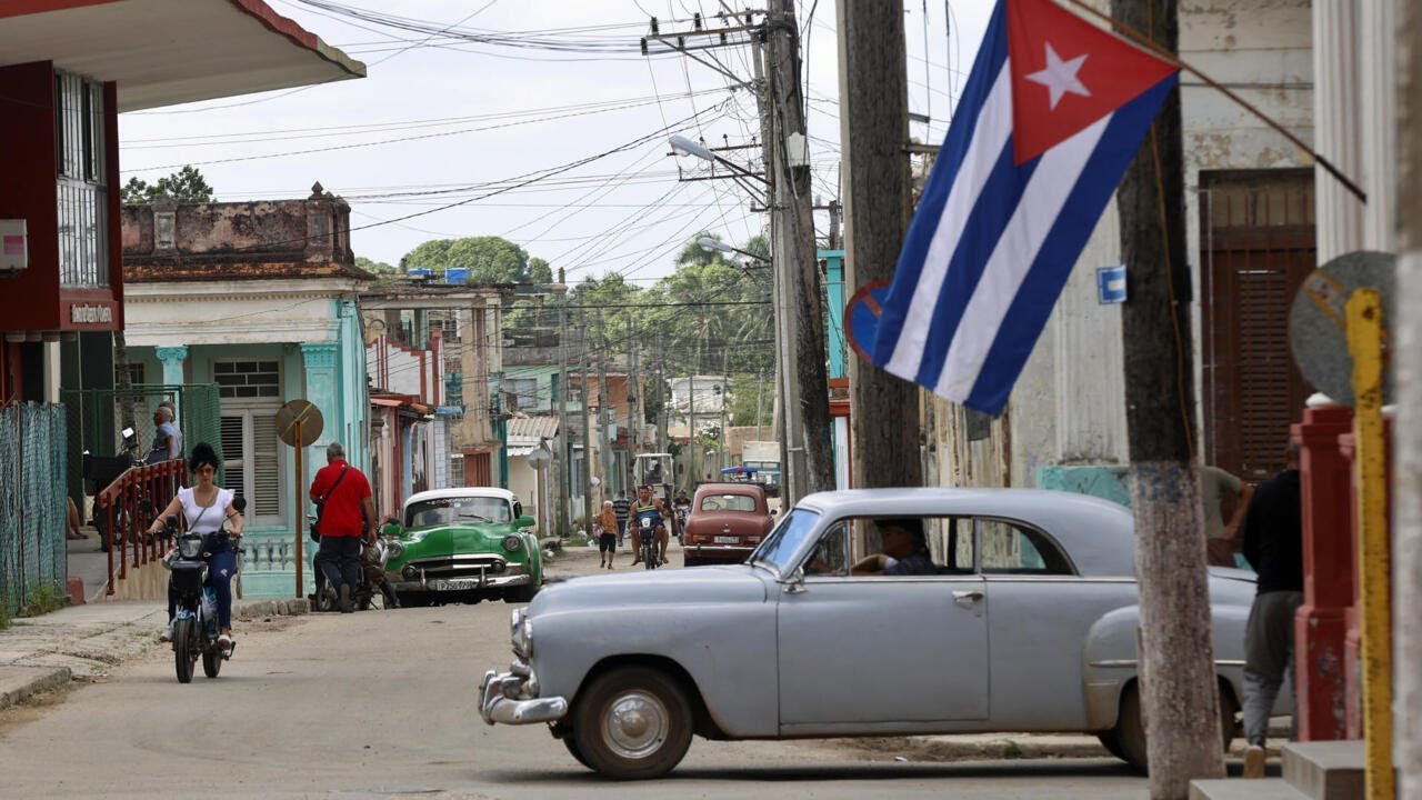 Calle en Cuba con coches clásicos y bandera cubana.