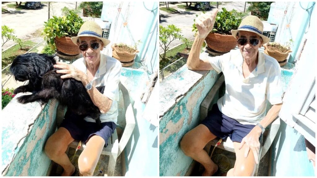 Hombre mayor en balcón con perro, sombrero de paja.