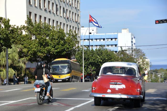 Calle con coches y bandera de Cuba ondeando.