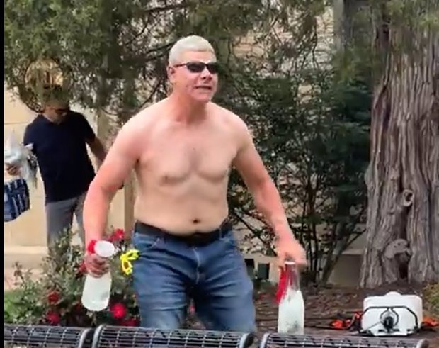 Hombre sin camiseta con botellas en un jardín.