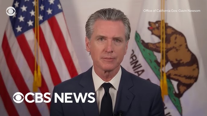 Hombre frente a banderas estadounidense y californiana.