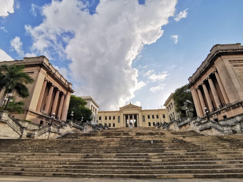 Escalinata y edificio histórico bajo nubes y cielo azul.