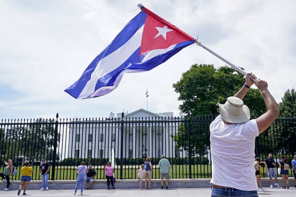 Persona con bandera cubana frente a edificio blanco