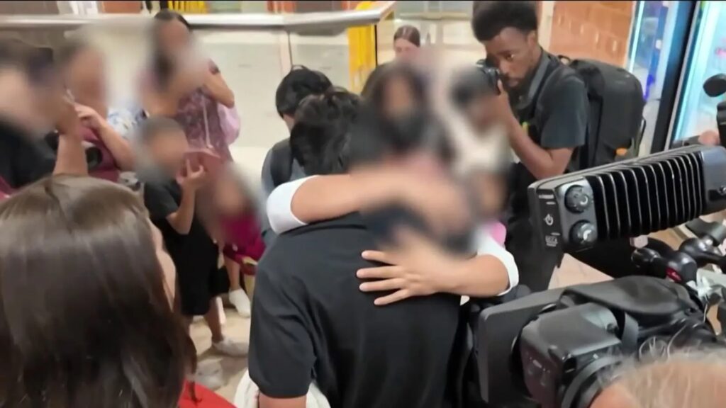 Reunión familiar emotiva en aeropuerto con cámaras presentes.