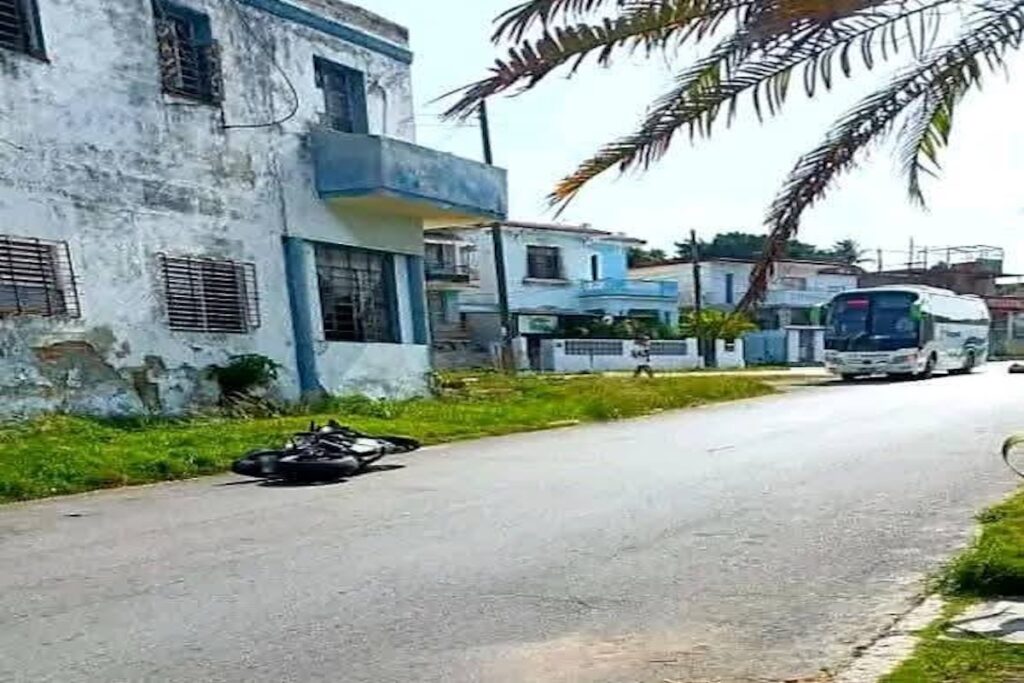 Motocicleta caída frente a edificio y autobús pasando