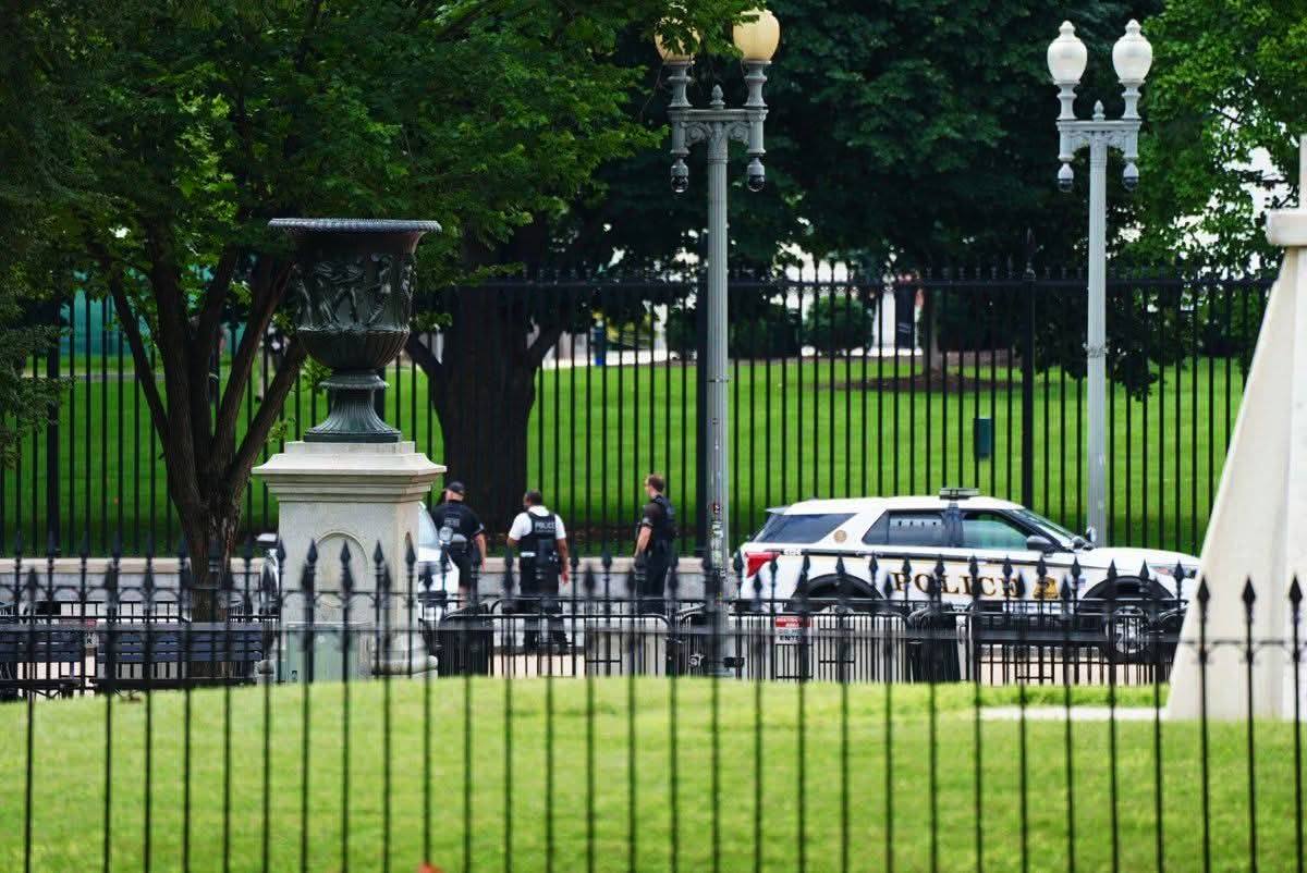 Policía frente a valla y jardín verde.