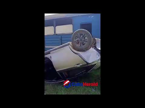 Coche volcado junto a edificio azul.