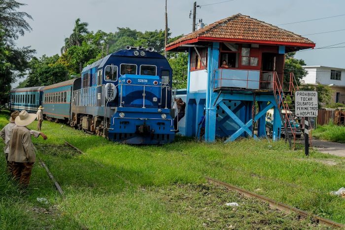 Tren azul pasando por una estación rural con señal.
