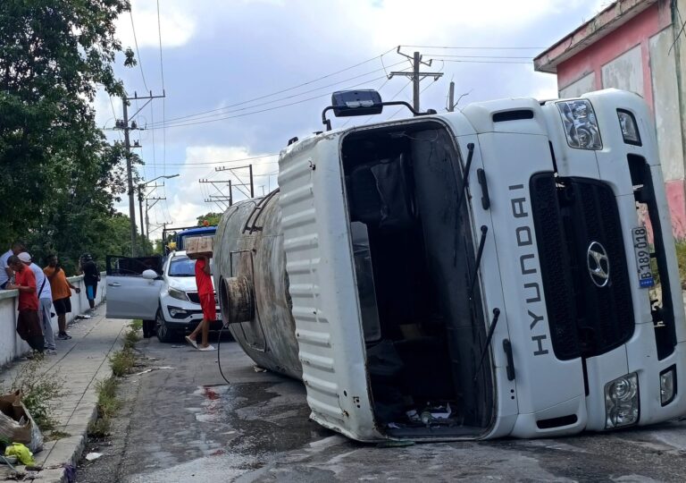 Camión volcado en la carretera con personas alrededor.
