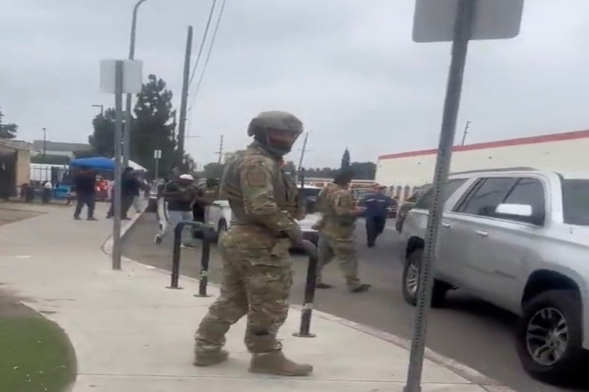 Militares en calle junto a vehículo blanco.