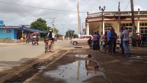Calle con charcos, bicicletas, personas y coches antiguos.