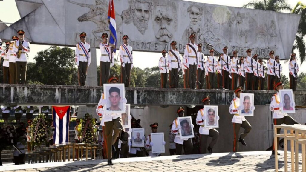 Militares cubanos en ceremonia fúnebre portando retratos de fallecidos.