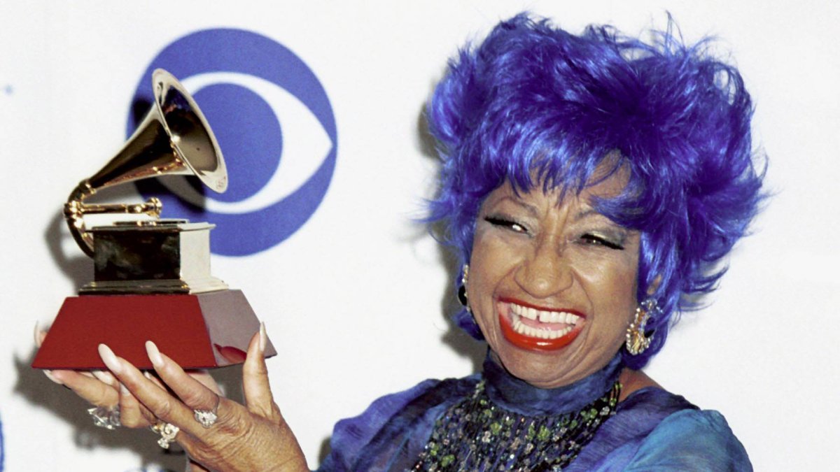 Celia Cruz sonriendo con peluca azul y un premio Grammy.