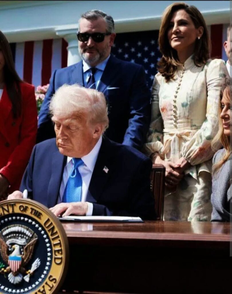 Donald Trump firmando un documento con Ted Cruz detrás.