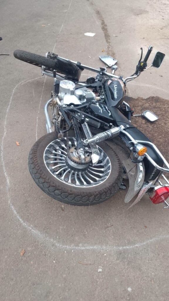 Motocicleta negra accidentada tumbada en el suelo sobre asfalto.