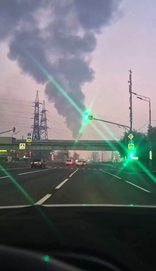 Columna de humo negro sobre carretera urbana al atardecer.