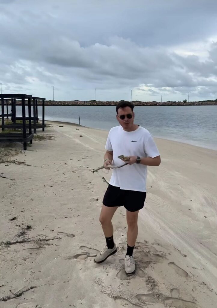 Hombre con camiseta blanca en una playa bajo cielo nublado.