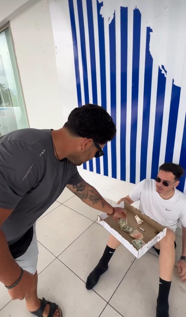 Hombre cogiendo billetes de una caja que sostiene otro hombre.
