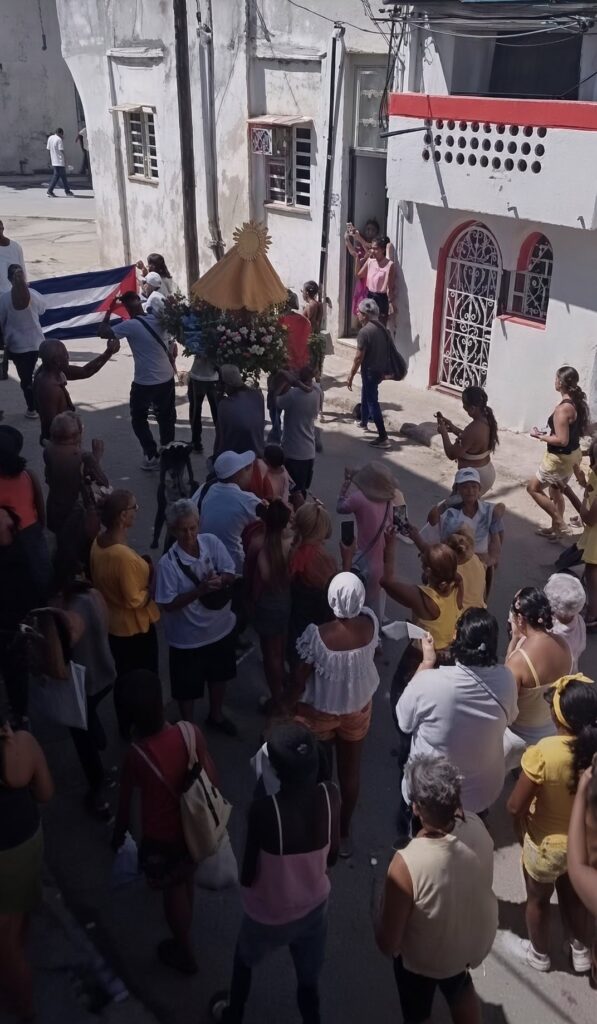 Multitud en procesión religiosa con la bandera de Cuba.