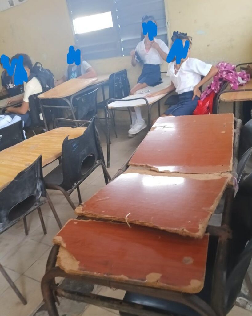 Estudiantes en un aula con pupitres antiguos y deteriorados.