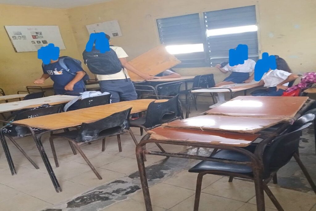 Estudiantes en un aula con pupitres de madera y mochilas.