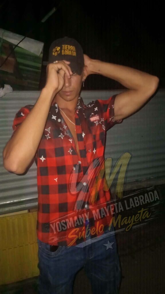 Joven posando con gorra negra y camisa roja de cuadros.