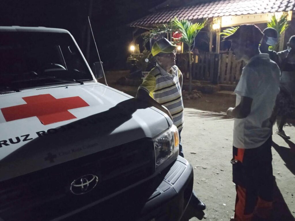 Hombre junto a vehículo de la Cruz Roja por la noche.