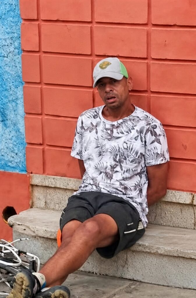 Hombre sentado frente a una pared de ladrillos rojos.