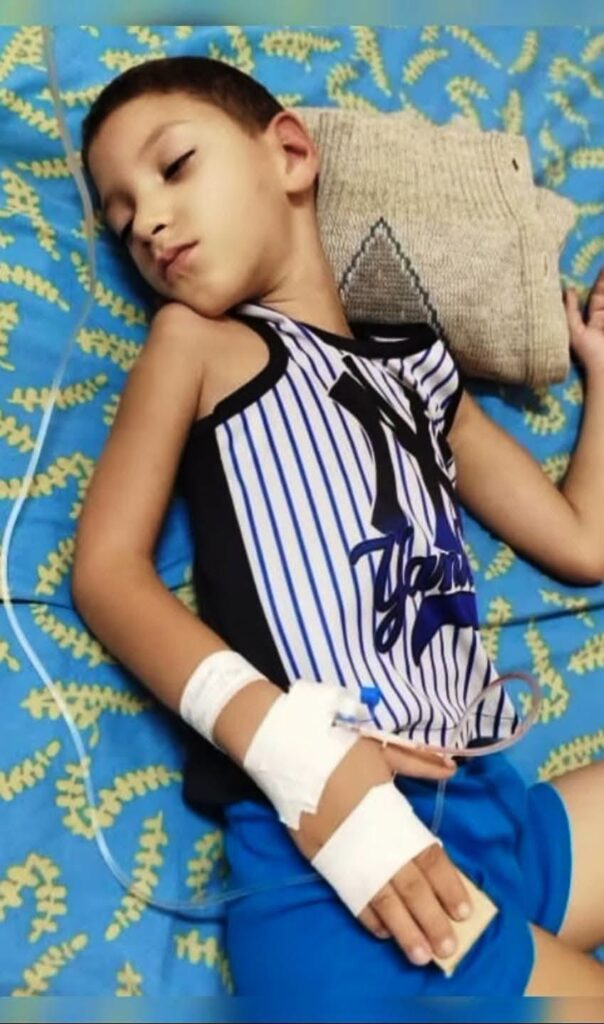 Niño durmiendo en cama de hospital con vía intravenosa.