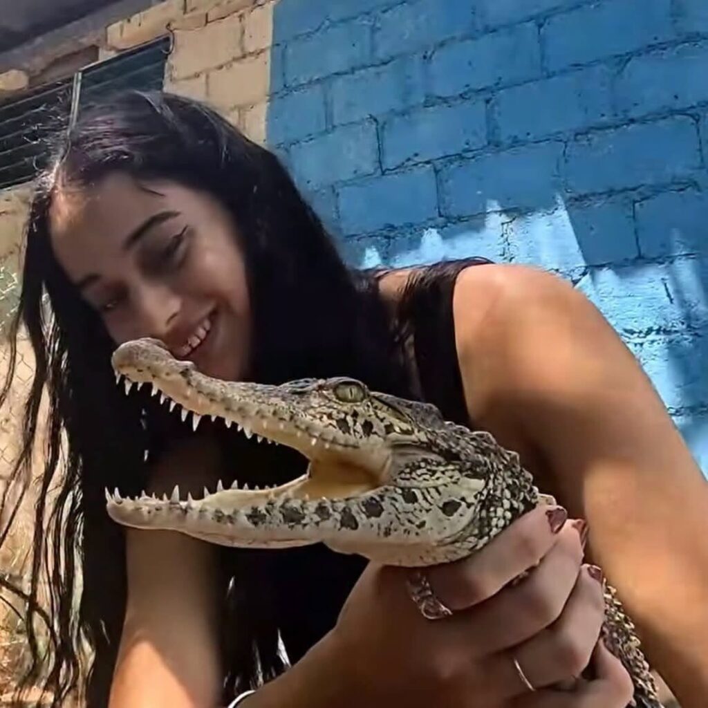 Joven sonriente sosteniendo un pequeño cocodrilo con la boca abierta.