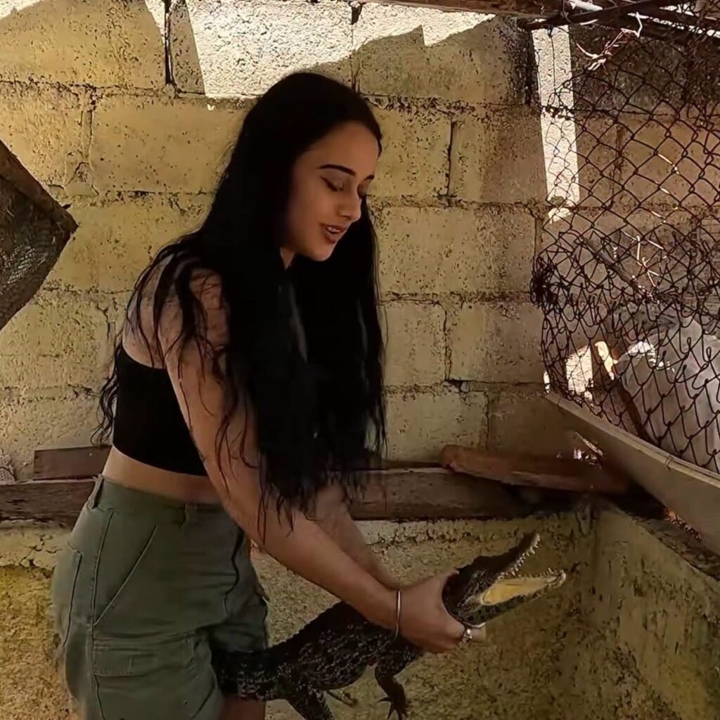 Mujer sosteniendo un pequeño cocodrilo con la boca abierta.