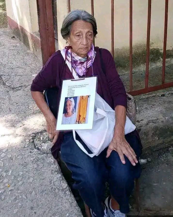 Mujer mayor sentada sosteniendo un cartel con una fotografía.