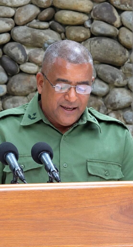 Hombre con uniforme militar verde hablando ante micrófonos.