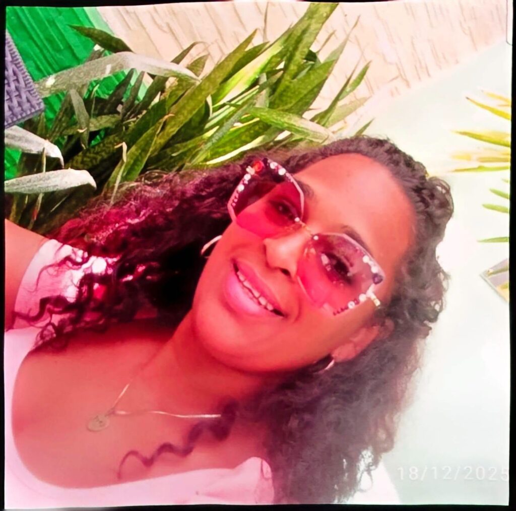 Mujer con pelo rizado y gafas de sol rosas sonriendo.
