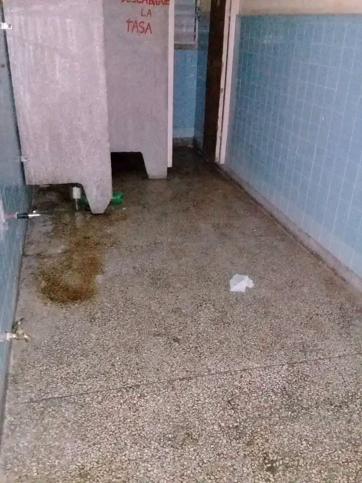 Baño público descuidado con paredes de azulejos azules y suelo sucio.