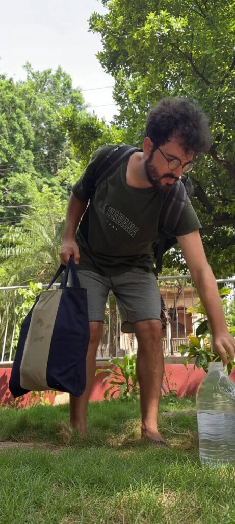 Hombre con gafas agachado en el césped con una garrafa.