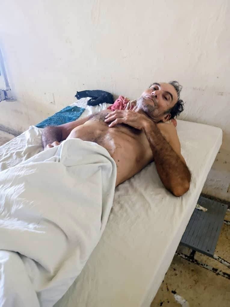 Hombre barbudo descansando en una camilla de hospital básica.