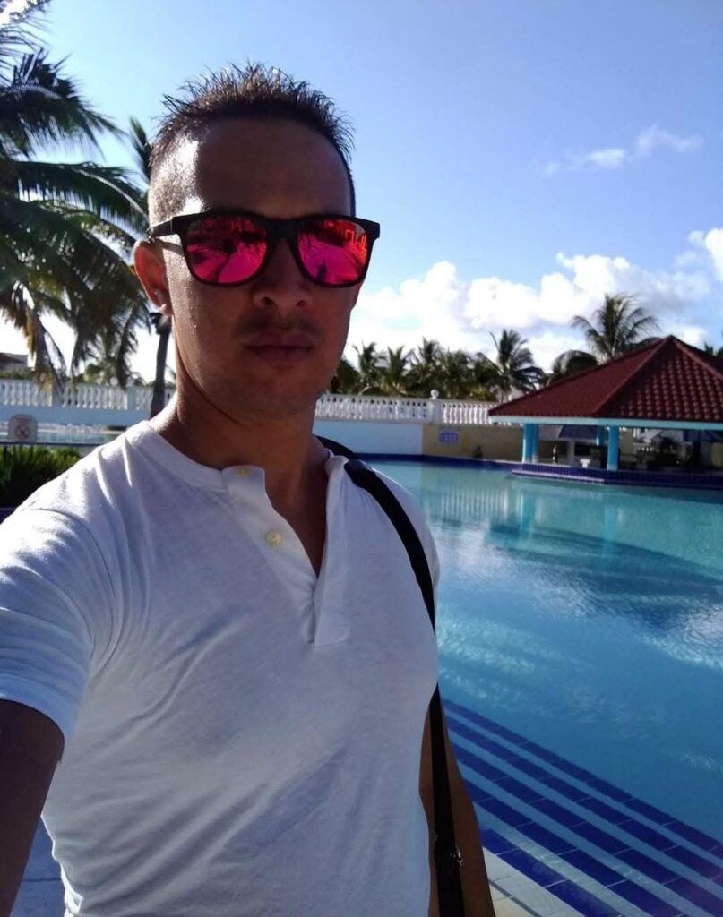 Hombre con gafas de sol frente a una piscina tropical.