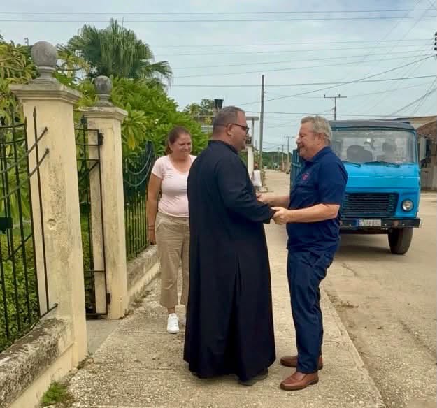 Sacerdote y hombre estrechando la mano en una calle.